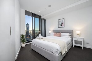 A modern hotel room with a large bed, a city view, a small bedside table, and a potted plant. - Level 50 Ocean View, Free Parking (Melbourne)