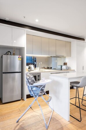 A modern kitchen with white cabinetry, a stainless steel refrigerator, a built-in oven, and a small island with a sink. - Level 50 Ocean View, Free Parking (Melbourne)