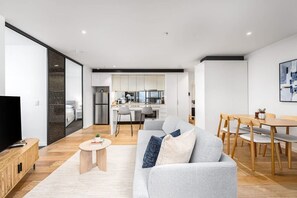 Ein modernes Wohnzimmer mit einem grauen Sofa, einem Holztisch und einem Essbereich mit Holzstühlen und einem Tisch.