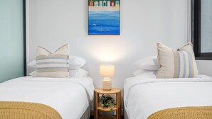 Et hotelværelse med to senge, et natbord med en lampe, et billede i ramme på væggen og et vindue.