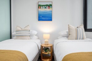 Ein Hotelzimmer mit zwei Betten, einem Nachttisch mit Lampe, einem gerahmten Bild an der Wand und einem Fenster.
