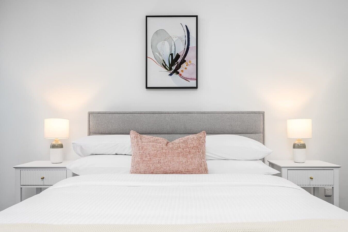 A bedroom with a large bed, two bedside tables with lamps, and a framed abstract artwork on the wall.