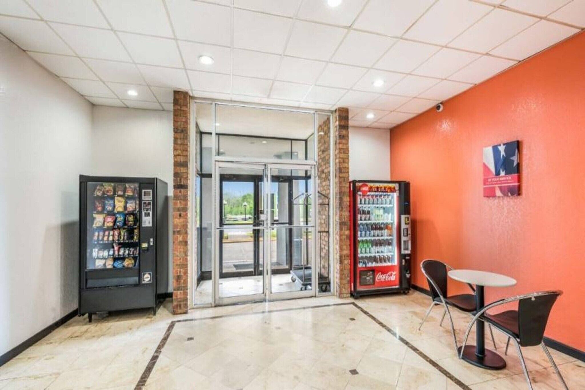 A lobby area with a vending machine, a glass door entrance, and a seating area with a table and chairs.
