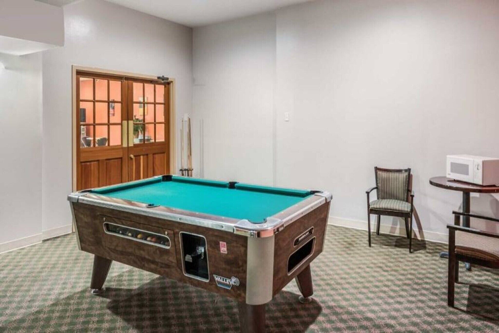 A pool table in a room with a door, a chair, and a microwave.