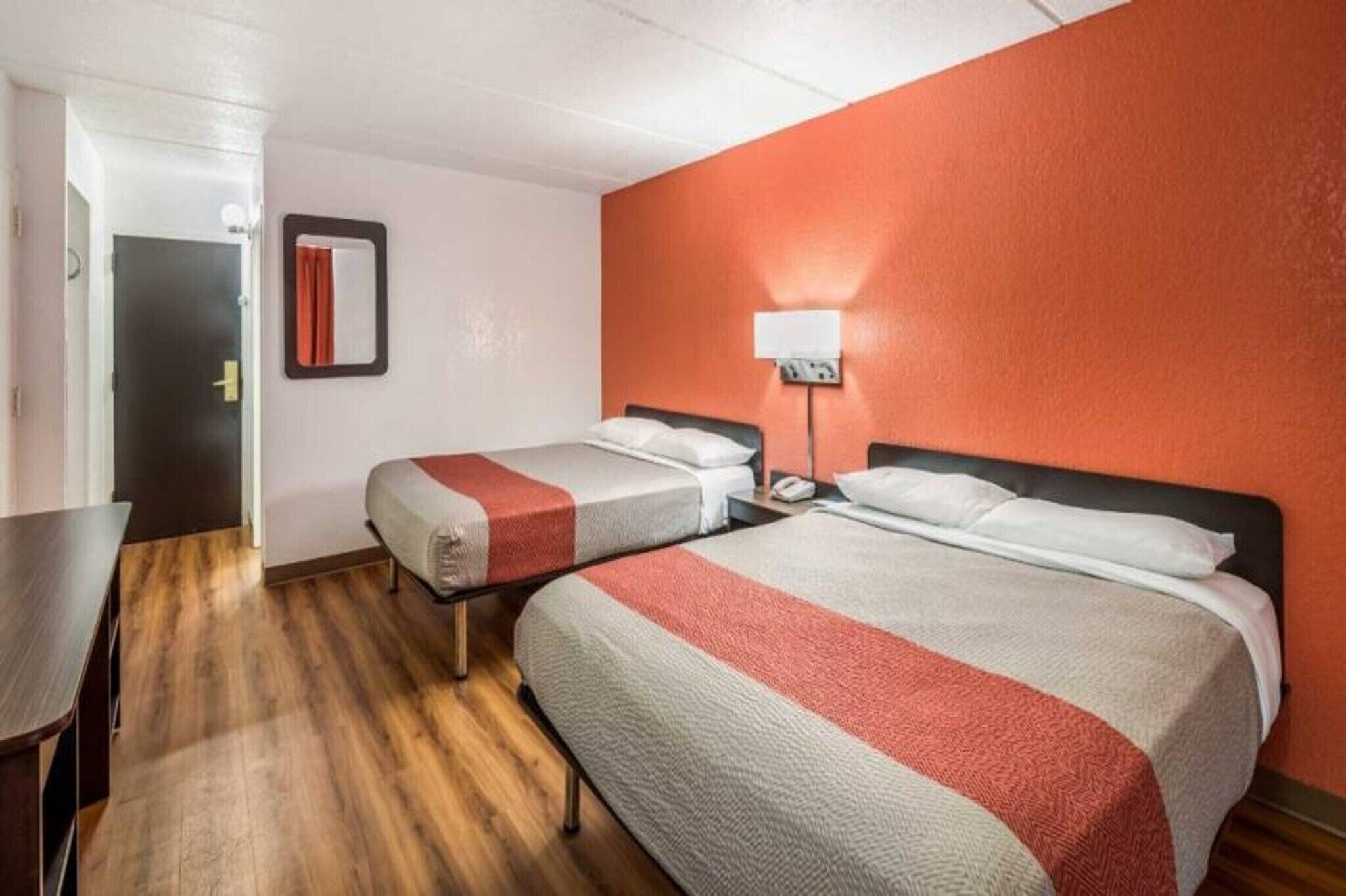 Una camera d'albergo con due letti, una scrivania e una porta.