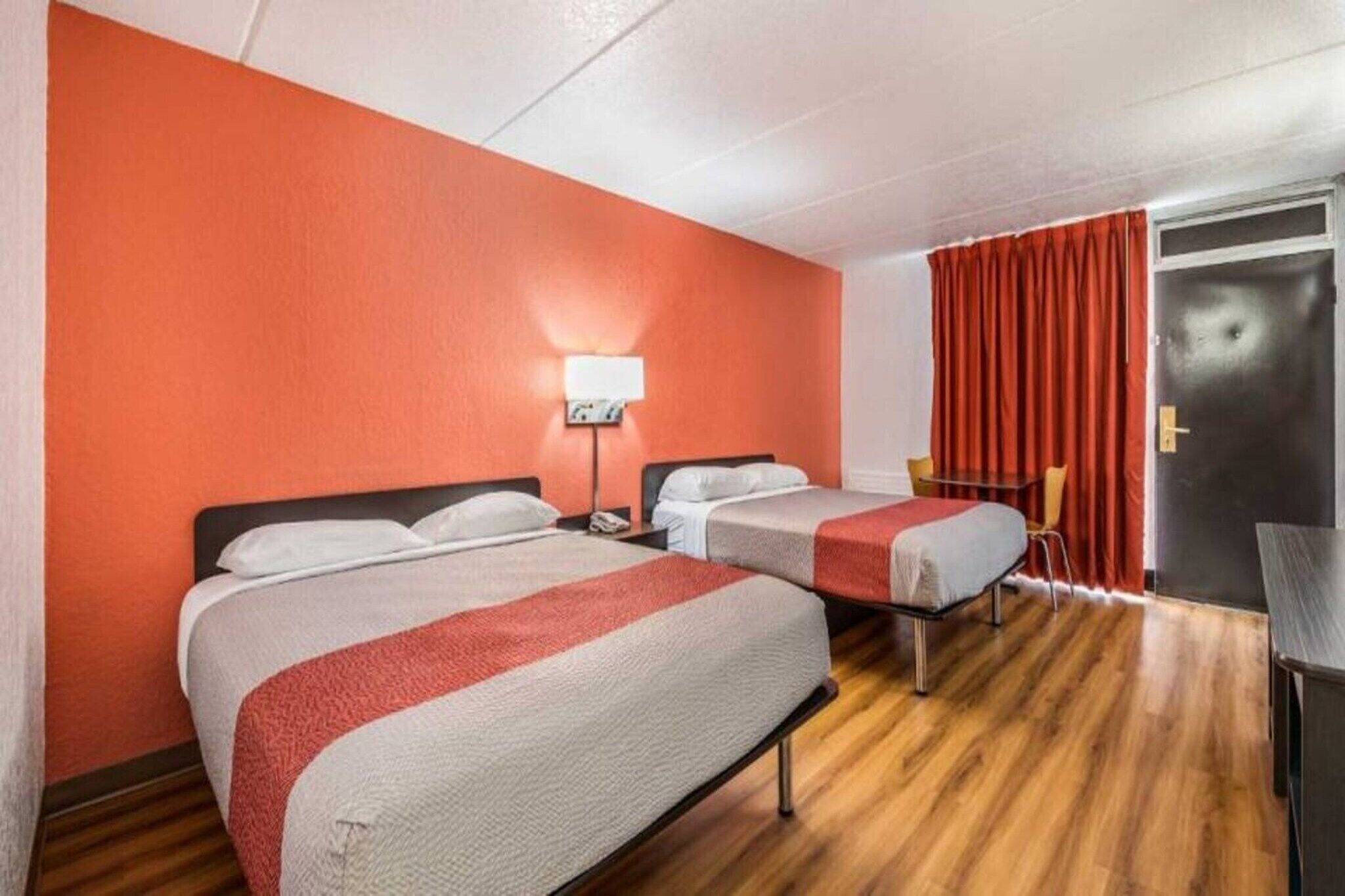 A hotel room with two beds, a desk, a chair, and a door.