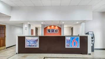 A hotel reception desk with a number 6 sign, a framed quote, and an ATM machine.