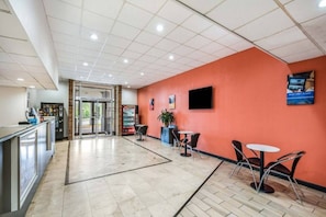 A lobby with a reception desk, a seating area with tables and chairs, and a red wall with a poster. - 1 King Bed | Non-Smoking, Micfridge (HENDERSON)