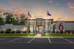 A building with a large number '6' on the facade, two flags, and a parking lot. - 1 King Bed | Non-Smoking, Micfridge (HENDERSON)
