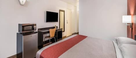 A hotel room with a bed, a desk with a computer, a television, and a microwave.