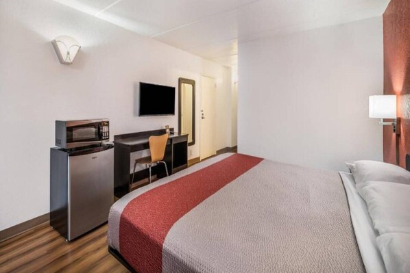 A hotel room with a bed, a desk with a computer, a television, and a microwave.