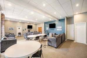 A spacious room with a round table, sofas, and a flat-screen TV mounted on the wall.