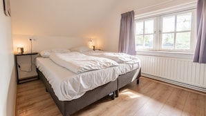 Ein Schlafzimmer mit einem Bett, Nachttischlampen, einem Fenster mit Vorhängen und einer Heizung.