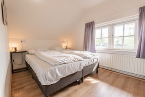Ein Schlafzimmer mit einem Bett, Nachttischlampen, einem Fenster mit Vorhängen und einer Heizung.
