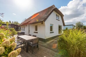 Ein weißes Haus mit einem Strohdach, einer Holzterrasse und einem Tisch mit Stühlen.