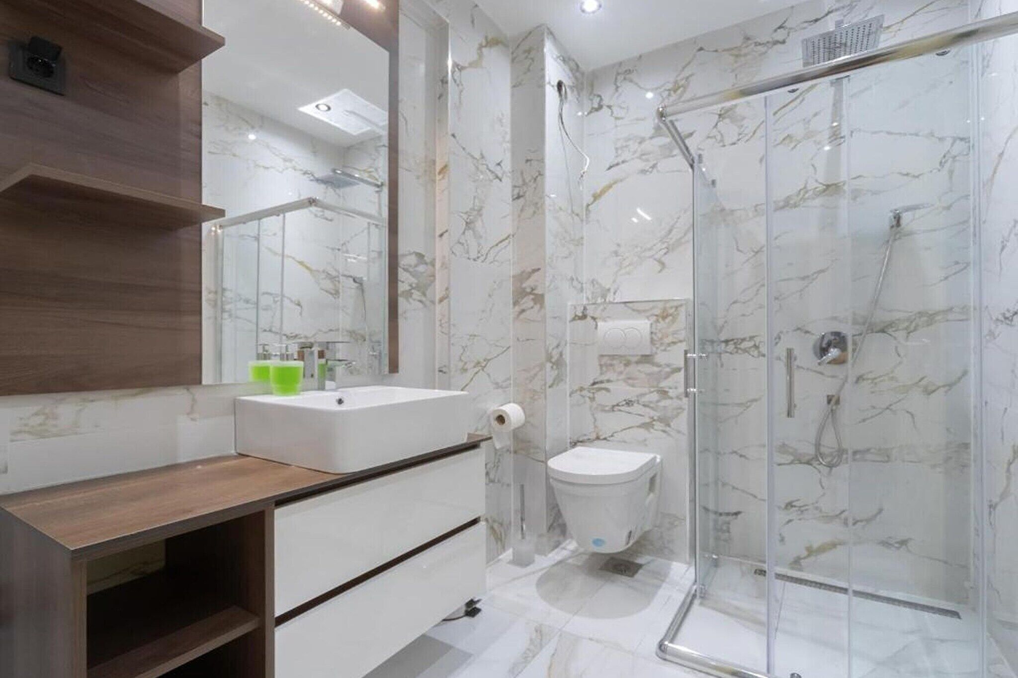 Ein modernes Badezimmer mit einer Marmerdusche, einem Holzbadezimmer-Waschtisch und einem Glaskabinenttoilette.