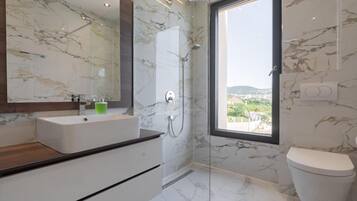 A modern bathroom with a marble shower, a large window, and a view of the city.