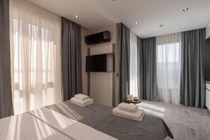 A hotel room with a large bed, a flat-screen TV mounted on the wall, and a small table with a tray. - Hotel D'Iman - Classic Triple Room with Sea View and Balcony (302) (Dobra voda)