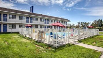 A motel with a swimming pool, fenced area, and a building with multiple windows and doors.