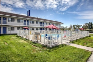 A motel with a swimming pool, fenced area, and a building with multiple windows and doors.