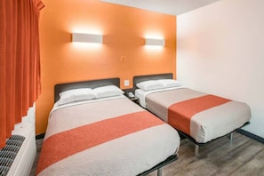 A hotel room with two beds, each with a white and orange bedspread, and a red curtain on the left.