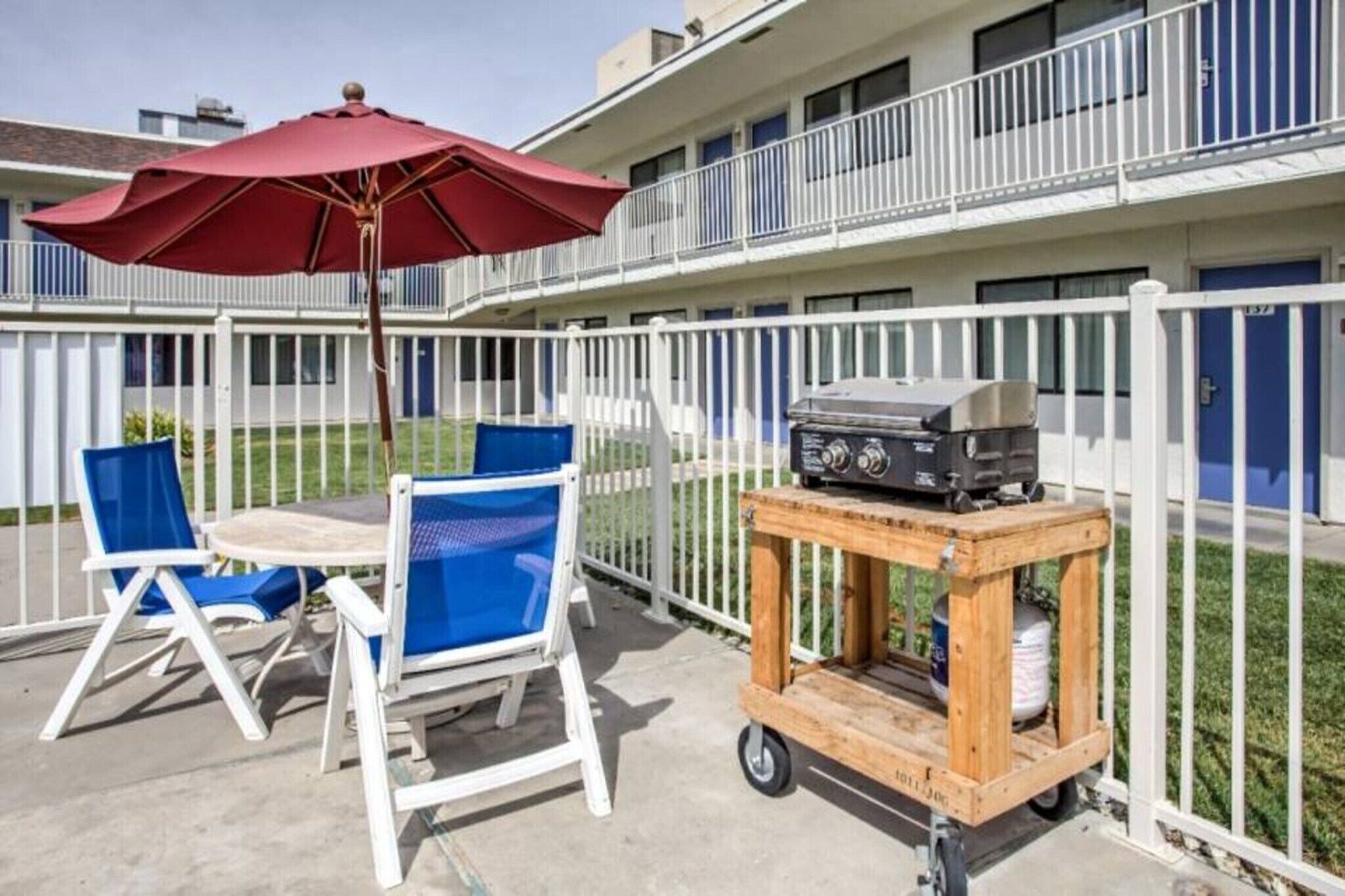An outdoor patio with a table and chairs, a grill cart, and a red umbrella.