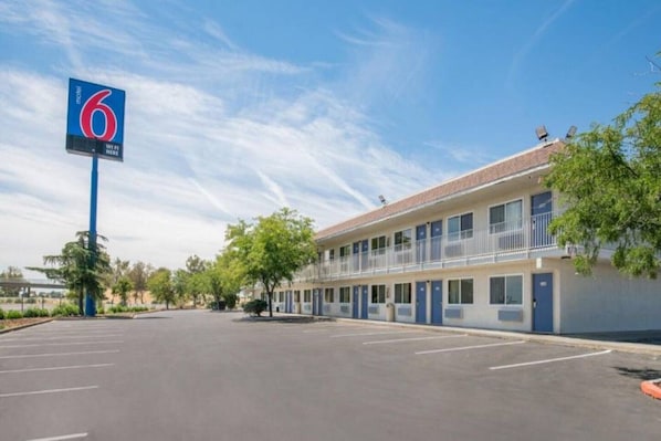 A motel with a large sign indicating the number 6. It has a parking lot in front and a building with multiple rooms.