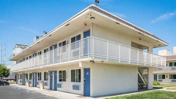A two-story motel with a balcony on the upper floor, a parking lot, and a clear sky.