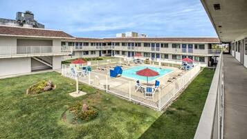 A hotel with a fenced outdoor pool area, multiple balconies, and a well-maintained lawn.