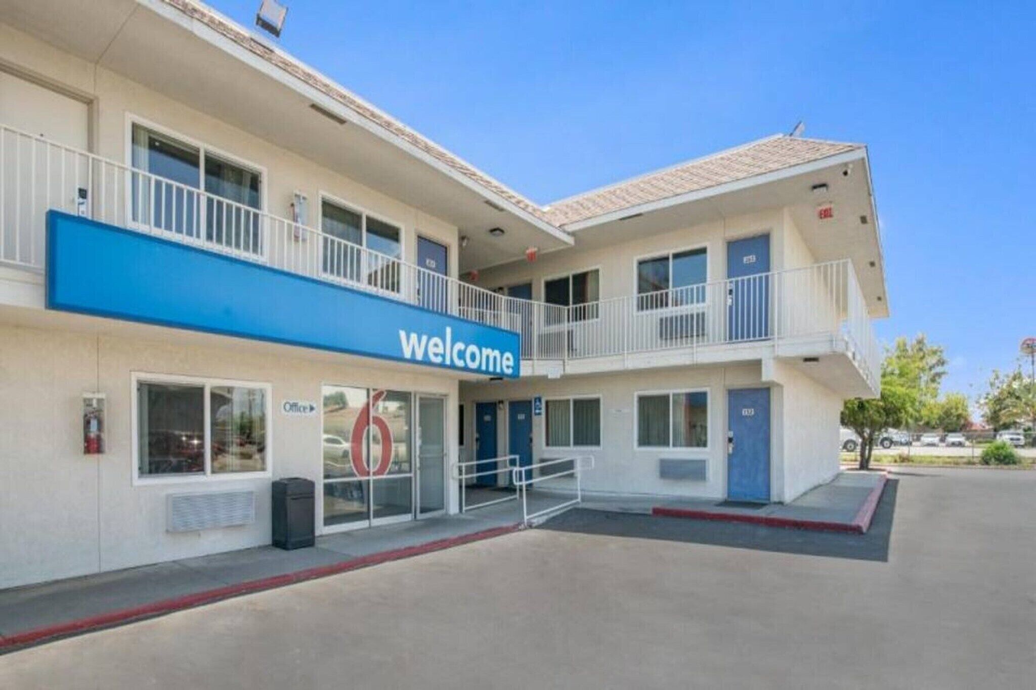 A two-story motel with a 'Welcome' sign, a visible office, and a parking lot.