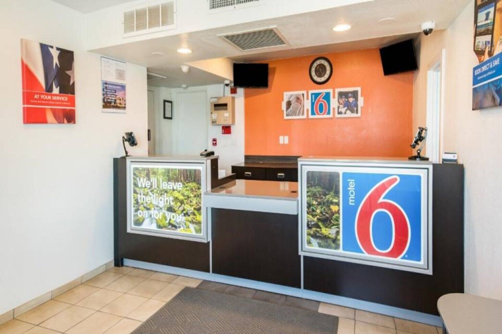 A hotel reception desk with a large sign reading '6 Motel' and a poster with a forest image and text.