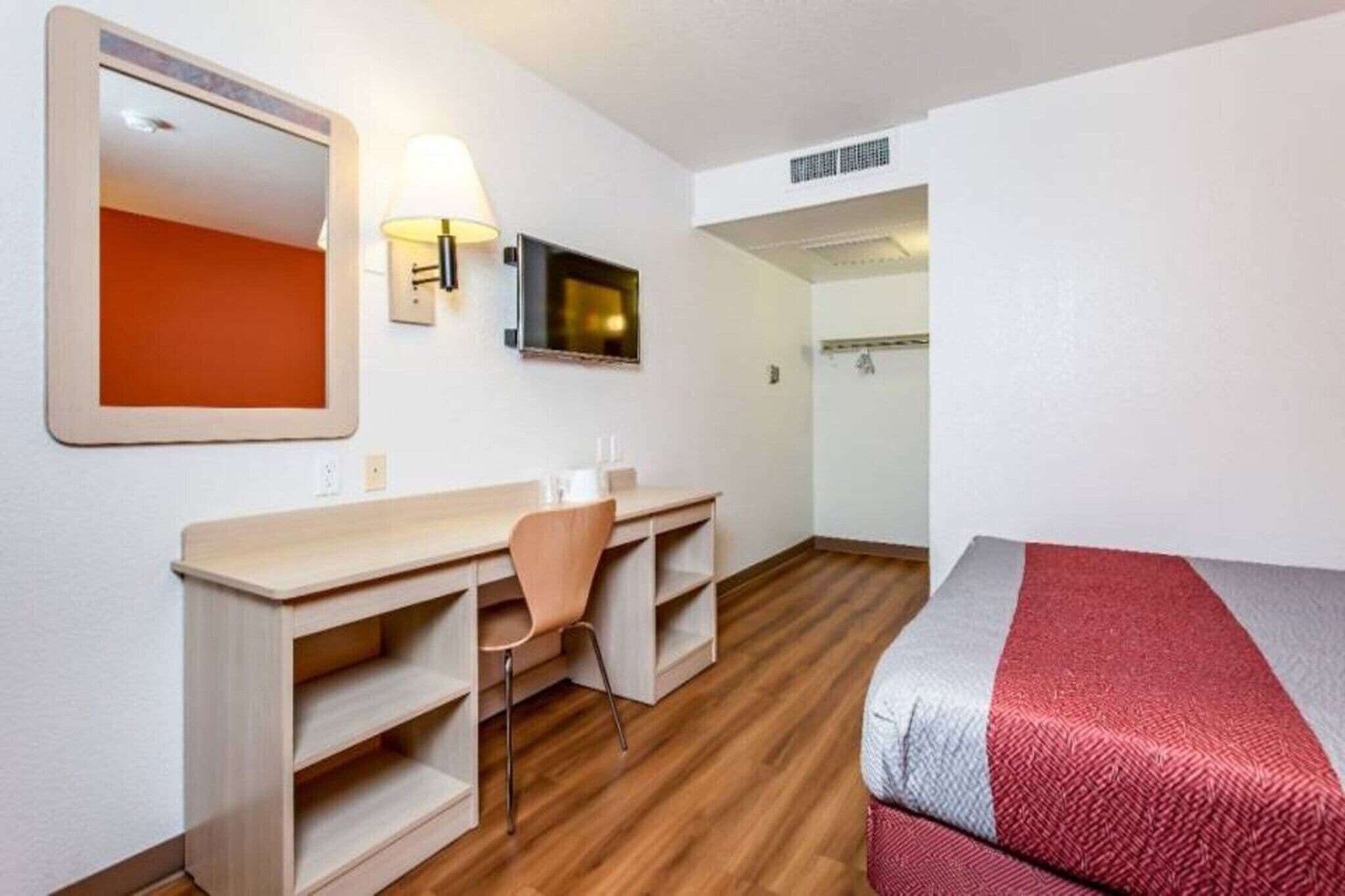 A hotel room with a bed, desk, chair, and a television.
