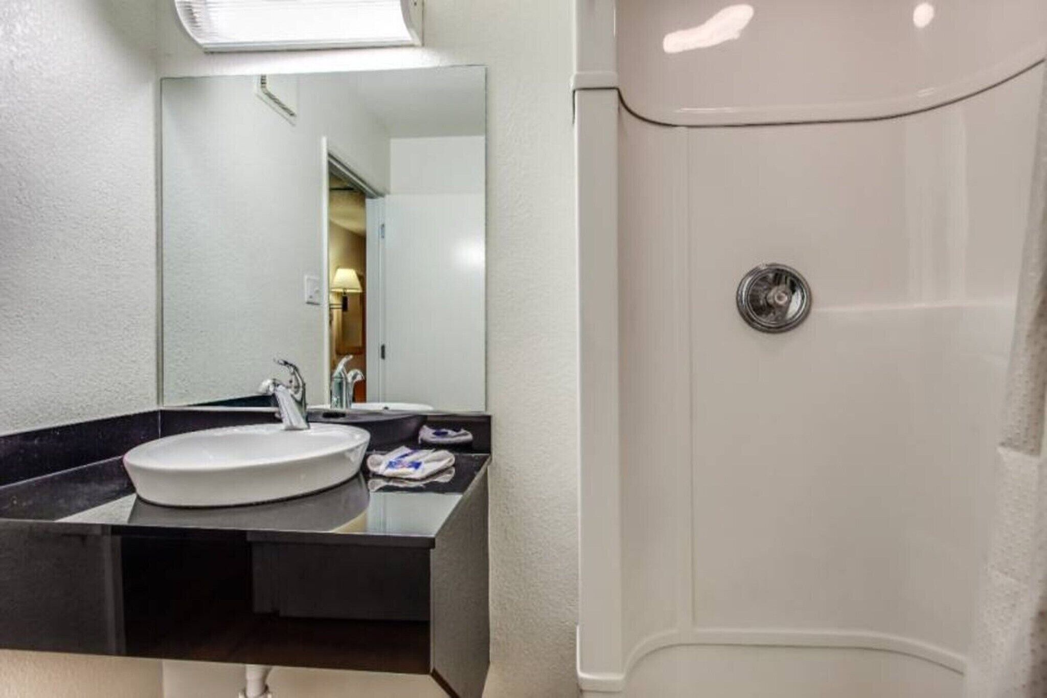 A bathroom with a sink, mirror, and shower.