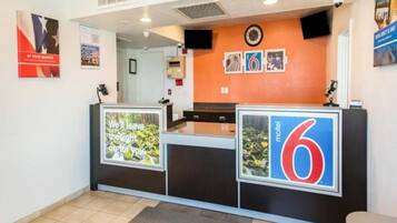 Ein Hotelrezeptionstresen mit einem großen Schild, auf dem '6 Motel' steht, und einem Poster mit einem Waldbild und Text.