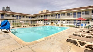 A swimming pool with lounge chairs and umbrellas, surrounded by a building with multiple balconies. - 1 Queen Bed | ADA/RI Shower/Non-Smoking (Williams)