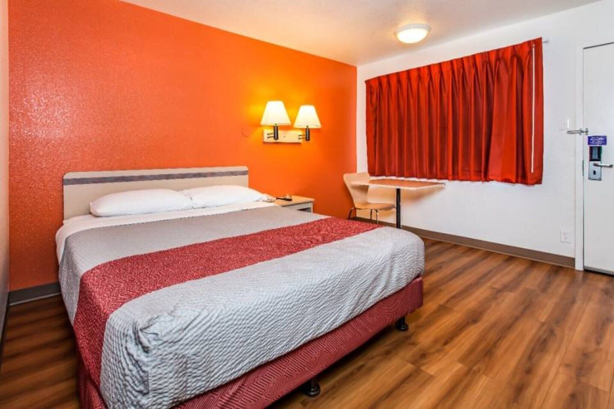 Hotellihuone, jossa on sänky, työpöytä, tuoli ja punainen verho.