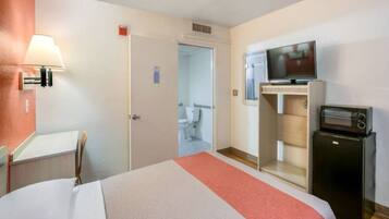 A hotel room with a bed, a television, a small refrigerator, and a bathroom visible through an open door.