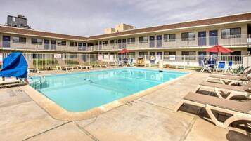 A swimming pool with lounge chairs and umbrellas, surrounded by a building with multiple balconies.
