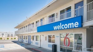 Un motel con un llamativo letrero de 'welcome', un estacionamiento y un edificio con varias entradas.