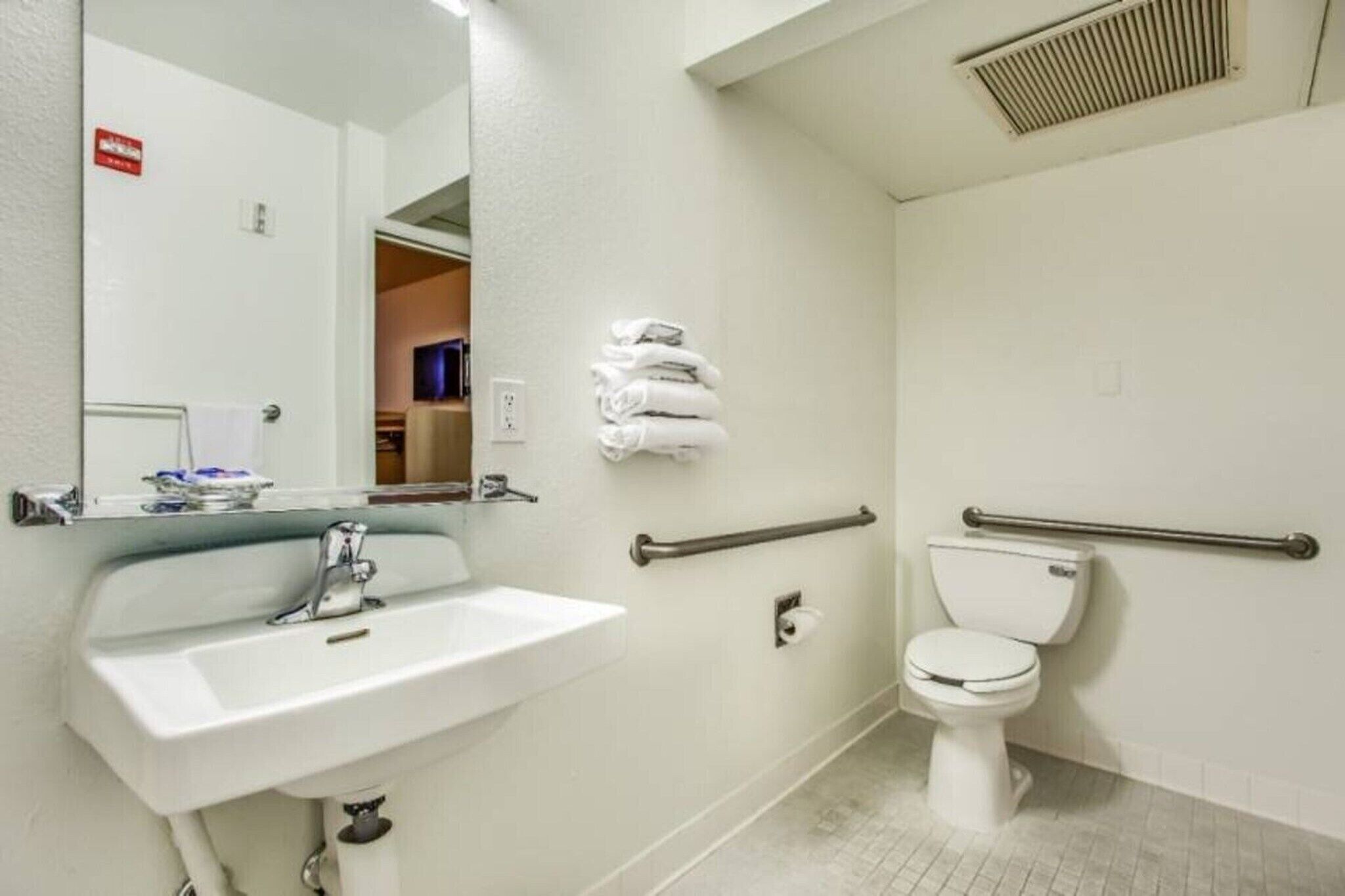 A hotel bathroom with a sink, toilet, and handrails.