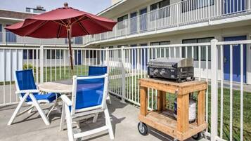 An outdoor patio with a table and chairs, a barbecue grill on a cart, and a red umbrella.