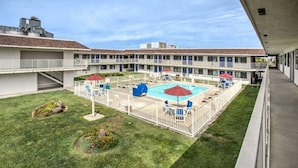 Un hotel con piscina, mobiliario exterior y césped cuidado.