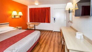 A hotel room with a bed, a desk, a chair, a red curtain, and a wall-mounted lamp. - Elegant Queen Bed|Pool|Free Parking (Williams)