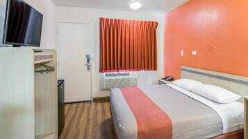 A hotel room with a bed, a desk, a television, and an air conditioning unit.
