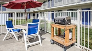 An outdoor patio with a table and chairs, a barbecue grill on a cart, and a red umbrella. - Elegant Queen Bed|Pool|Free Parking (Williams)
