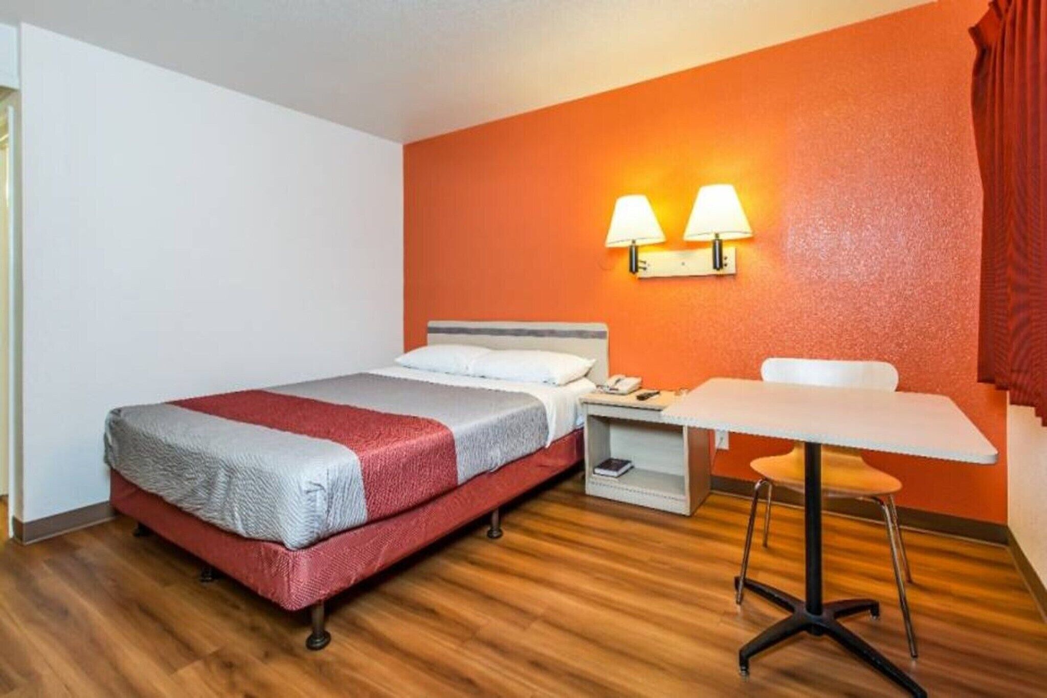 A hotel room with a bed, bedside table, lamp, and a small table with a chair.