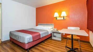 A hotel room with a bed, bedside table, lamp, and a small table with a chair.