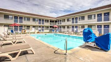 A hotel pool area with lounge chairs and umbrellas, surrounded by a multi-story building with balconies.