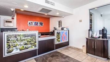 Zona de recepción de un hotel con mostrador, estación de café y un cartel con el número 6.