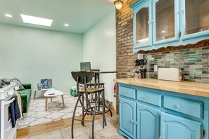 A kitchen with blue cabinets, a brick accent wall, and a dining area with a green sofa and a small table. - Walk to HBLR & Liberty State Park: Jersey City Apt (Jersey City)